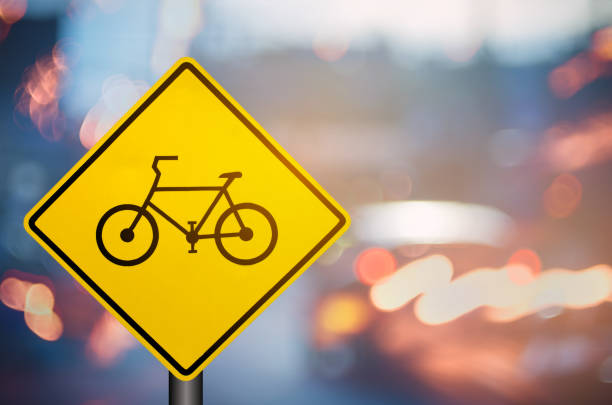 Bicycle warning sign on blur traffic road with colorful bokeh light abstract background. Copy space of transportation and travel concept. Retro tone filter effect color style.