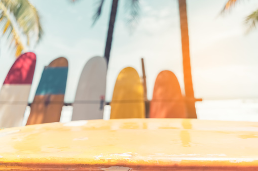 Copy space of yellow surface texture on blur colorful surfboard and palm tree at tropical beach background. Product present in nature sport. Vintage tone filter effect color style.