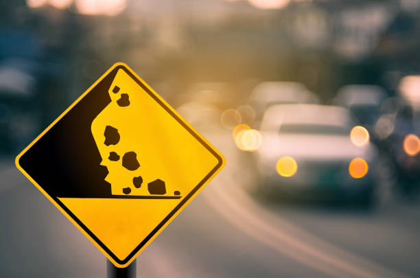 Falling stone warning traffic sign on blur road with colorful bokeh light abstract background. Copy space of travel and transportation concept. Vintage tone color filter style.
