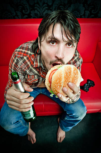 What do you want from me Young couch potato with burger, beer and videogame joystick brat burger stock pictures, royalty-free photos & images