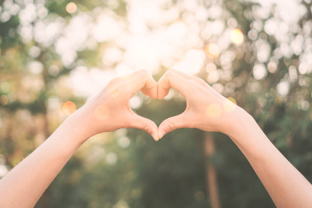istock Female hands heart shape on nature bokeh sun light flare and blur leaf abstract background. Copy space of happy love and freedom concept. Vintage tone filter color style. 1157486237