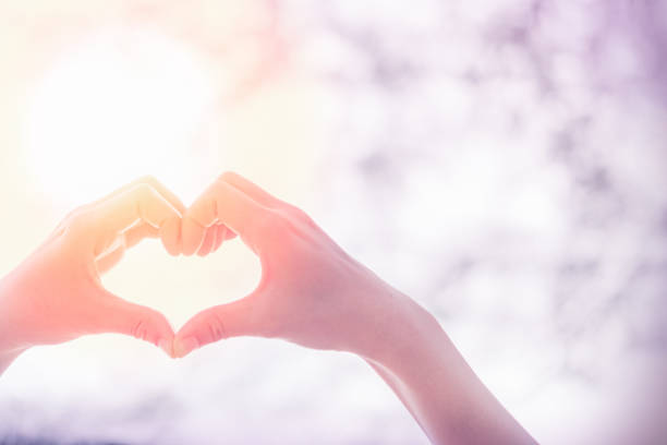 istock Female hands heart shape on nature bokeh sun light flare and blur leaf abstract background. Copy space of happy love and freedom concept. Vintage tone filter color style. 1157486238