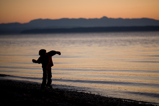 Silhouette of a boy skipping stones at dusk.
