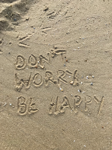Stock photo of writing drawn on sunny beach with Don't worry be happy words written in sand with stick, by sea waves, concept social media photo of handwriting letters in soft golden sand on Bournemouth beach, Dorset, England seaside coastline view