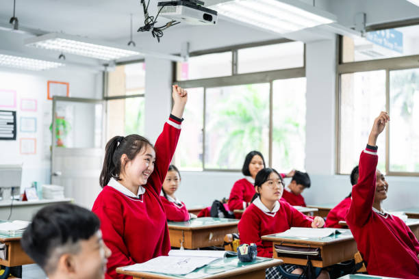 istock Cheerful schoolgirl with hand raised in classroom 1157499122