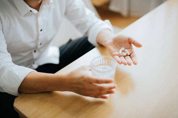 close up of man holding a glass of water and medication in his hand - vitamin pill pill medicine healthcare and medicine imagens e fotografias de stock