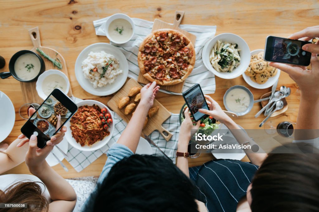 Grupo de amigos tomando fotos de comida en la mesa con teléfonos inteligentes durante la fiesta - Foto de stock de Influencer libre de derechos