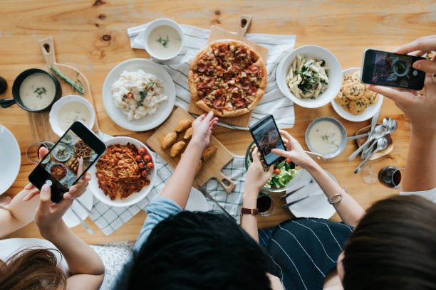 grupo de amigos que tomam retratos do alimento na tabela com os smartphones durante o partido - food photography - fotografias e filmes do acervo