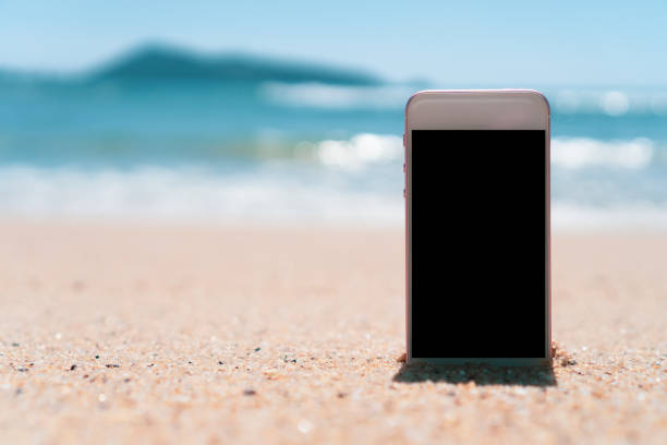 istock Smart phone on tropical sand beach with bokeh sun light wave texture background. Black copy space of technology and travel nature concept. Vintage tone filter effect color style. 1157500050