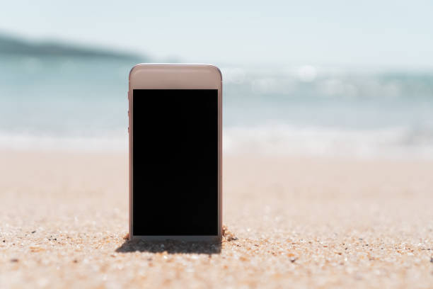 istock Smart phone on tropical sand beach with bokeh sun light wave texture background. Black copy space of technology and travel nature concept. Vintage tone filter effect color style. 1157500113