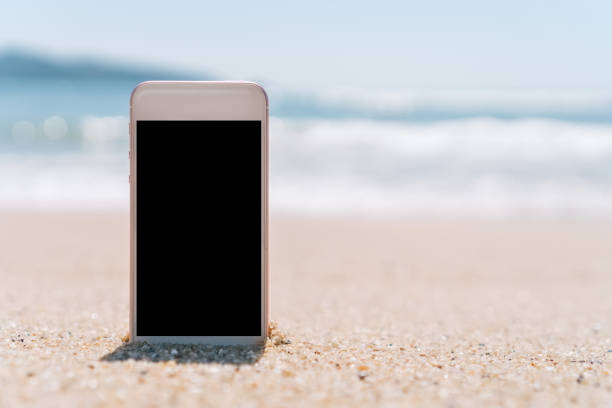 istock Smart phone on tropical sand beach with bokeh sun light wave texture background. Black copy space of technology and travel nature concept. Vintage tone filter effect color style. 1157500122