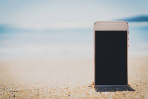 istock Smart phone on tropical sand beach with bokeh sun light wave texture background. Black copy space of technology and travel nature concept. Vintage tone filter effect color style. 1157500123