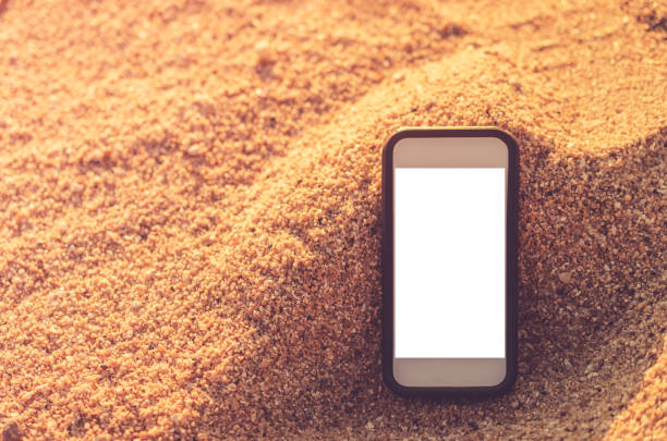 Smart phone on tropical sunset beach with bokeh light sand texture background. White copy space of technology and travel nature concept. Vintage tone filter effect color style.
