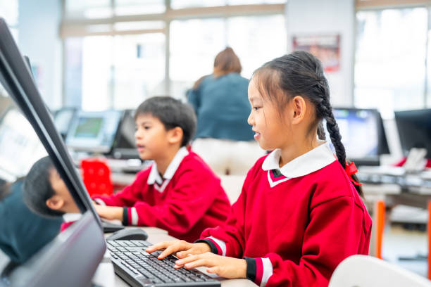 istock Cute schoolgirl learning computer by friend in lab 1157500166