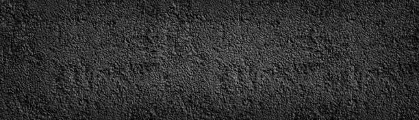 istock Black painted stone wall wide texture. Dark coarse pebbledash panoramic background 1157501035