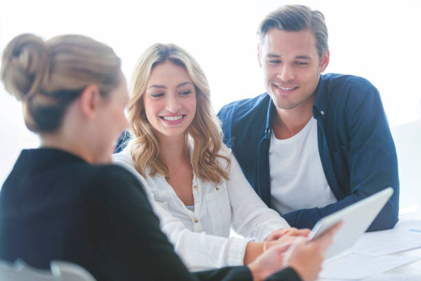 istock Real estate agent with couple looking through documents. 1157507694
