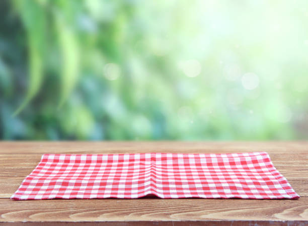 istock Red checkered picnic cloth on wooden tablue blurred green background. 1157518352
