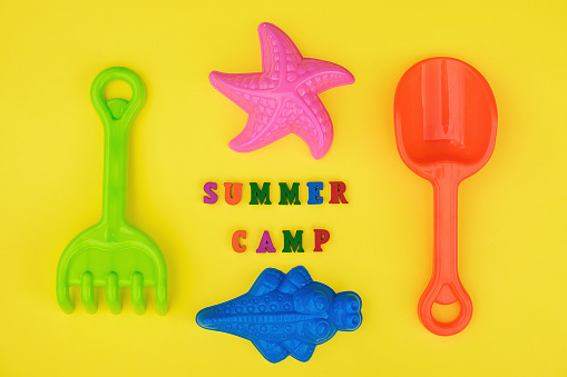 Text Summer camp and multicolored set children's toys for summer games in sandbox or on sandy beach on yellow background. Creative top view Flat lay Concept children's rest and development.