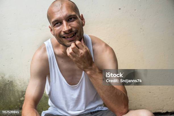 Joven Flaco Calva Anoréxica Positiva Y Feliz Sonriendo Hombre Sin Hogar Sentado En La Calle Urbana En La Ciudad O La Ciudad Cerca De La Pared Blanca Con Gran Sonrisa Concepto Documental Social Sin Hogar Foto de stock y más banco de imágenes de Sin techo