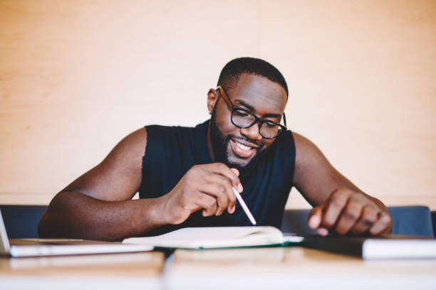 istock Smiling african american guy in eyewear spending time on autodidact reading information from education books, positive dark skinned businessman making plannings sitting at cafe interior with notepad 1157541045
