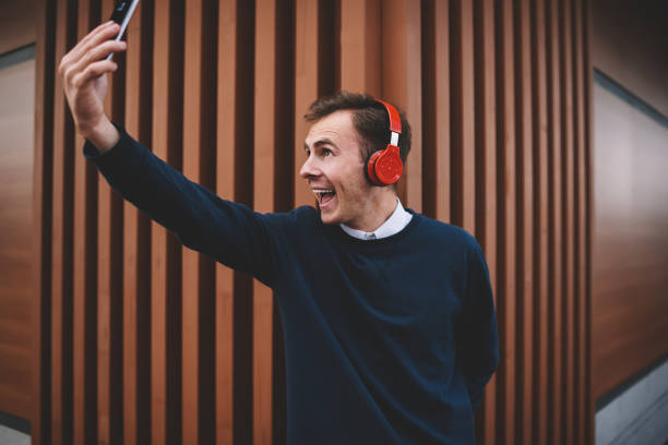 istock Handsome emotional male student having fun while making selfie on modern cellular camera for updating profile picture.Cheerful hipster guy fooling around during taking picture standing at street 1157542096