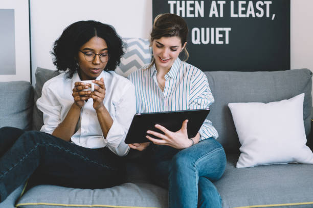 istock Two multicultural female friends watching and discussing new design collection on website on digital tablet connected to home internet enjoying leisure time on comfortable couch in stylish apartment 1157543217