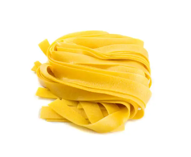 Raw yellow italian pasta pappardelle, fettuccine or tagliatelle close up. Egg homemade dry ribbon noodles, long rolled macaroni or uncooked spaghetti isolated