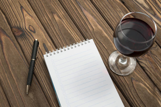 un cuaderno en una espiral, un bolígrafo, una copa de vino tinto sobre un fondo de mesa de madera. - wood texture audio fotografías e imágenes de stock