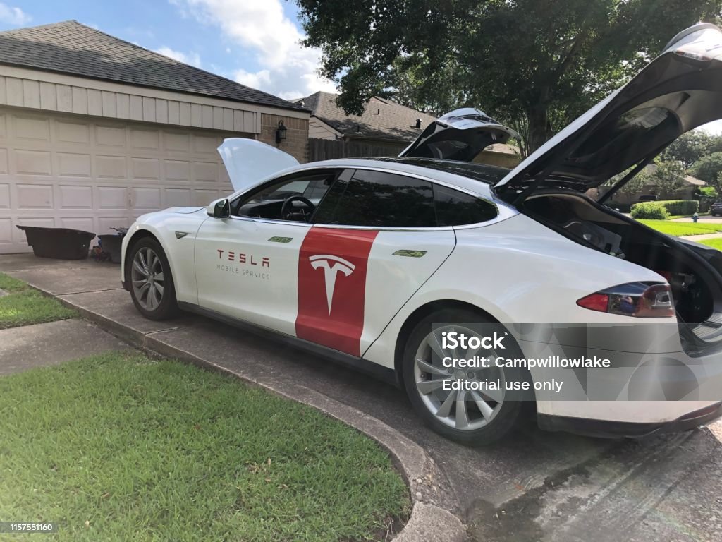 Tesla repair technician car in driveway doing repair May 25, 2019 - Houston, Texas - Tesla repair technician is in the driveway of a home doing an automotive repair.  The Tesla repair technician's car with the red Tesla logo is parked in the driveway. Tesla Model 3 Stock Photo