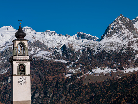 Antagnod, Aosta Valley, Italy - November 15, 2012: Bell tower with a copper roof, and the Monte Rosa massif in the background.