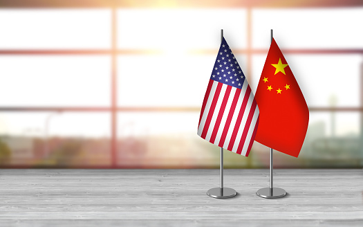 3D USA and chinese flags with metallic pole, standing together on a white wooden desk in front of sunny window background. With large copy space you can write your own titles effectively. Also you can use this compositon as square in social media channels like instagram etc.