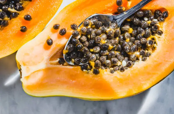 Papaya fruit cut in half with seeds on white marble background and sunbeam.