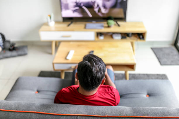 istock Back view of young man watching television in home 1157564448