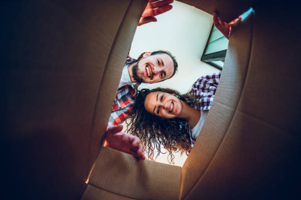 Happy young couple looking inside the box Happy young caucasian couple looking inside the cardboard box. receiving box stock pictures, royalty-free photos & images