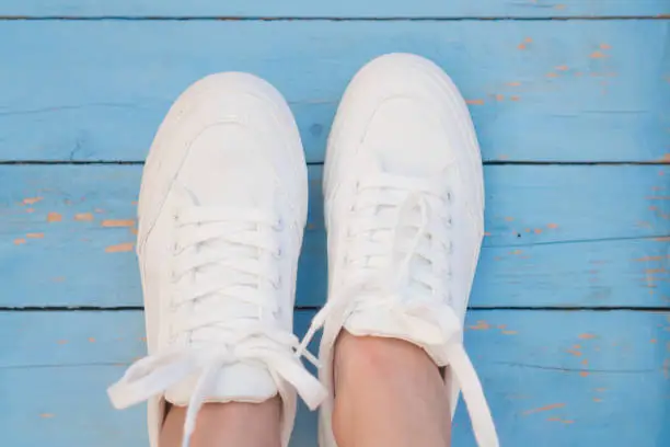 Photo of White women's sneakers on a blue boardwalk background. Clean white sneakers in the center of the frame on the blue wooden floor. Trend shoe onthe blue background witn copyspace