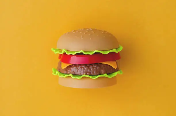 Photo of Toy burger with meat and salad on an orange background.