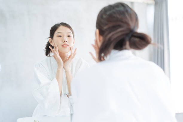 여성 스킨 케어. 젊은 아시아 여자 감동 그녀의 얼굴 과 찾고 에 거울 에 화장실 - bathtub women bathroom asian ethnicity 뉴스 사진 이미지