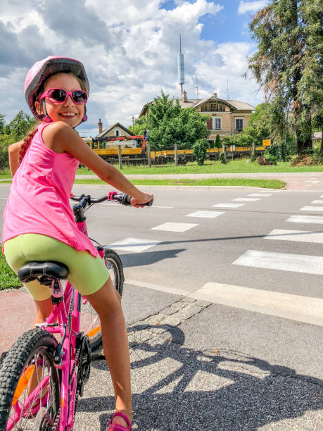 smiling little girl stopping at zebra crossing with her bicycle - helmet bicycle little girls child imagens e fotografias de stock