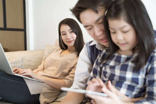 happy asian family spending time together on sofa in living room. family and home concept - laptop women child digital tablet imagens e fotografias de stock