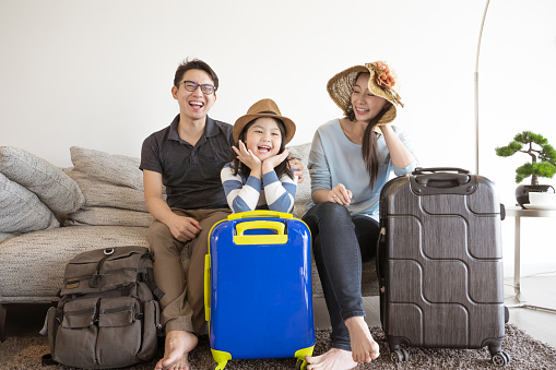 Happy Asian family is preparing for travel at home .Mom daughter and father are packing suitcases for the trip.