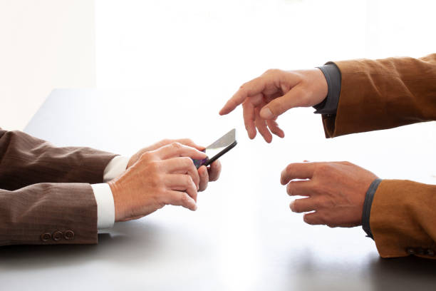istock Hands from two businessmen in conversation by a desk. One texting on a cell phone and the other pointing. Negotiating business or a job interview. - Image 1157577209