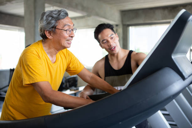 asian Senior man walking exercise on treadmill with Personal trainer workout in fitness gym . sport trainnig , retired , older , mature, elderly , smiling .rehab stock photo