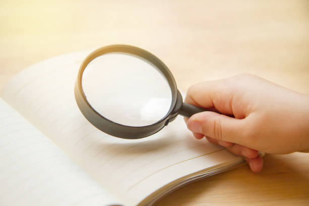 istock kid hand holding magnifier and blank book on wooden table 1157580460
