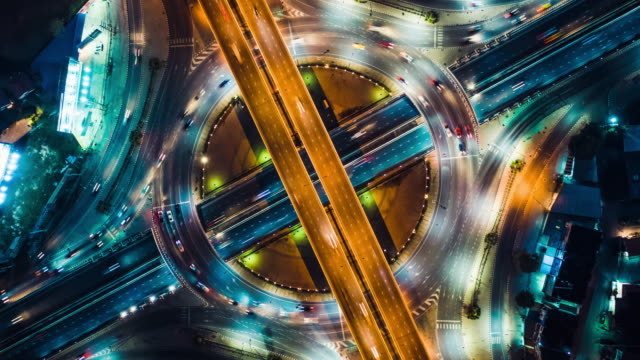 Top view hyperlapse time-lapse of car traffic at circle roundabout, 4K UHD drone zoom out aerial shot. Land transportation, urban cityscape, or advanced transport technology concept