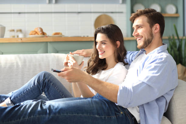 istock Young loving couple on sofa at home watching tv and laughing. 1157597321