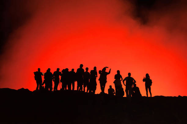 Tourists' silhouettes standing on the edge of Erta Ale Volcano, illuminated with red lava smoke Active shield volcano, erupting at night in Danakil Depression in Ethiopia, impressive natural phenomenon danakil depression stock pictures, royalty-free photos & images