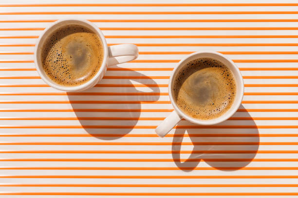 due tazze di caffè bianco sulla vista dall'alto del tavolo a strisce arancioni - morning coffee coffee cup two objects foto e immagini stock