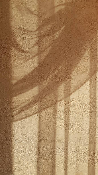 istock Soft shadows from elegant draped tulle curtain on rough textured plaster wall surface in shades of beige color. Shadow contours of textile folds. Sepia background. Light and shadow backdrop. 1157617653