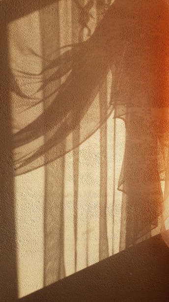 istock Shiny lightened shadows from draped tulle curtain on beige textured plaster wall surface. Contours of soft textile folds textures. Wavy and striped patterns background. Light and shadow backdrop. 1157617681