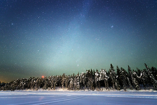 Night sky with lots of stars over a snowy landscape with a forest and a frozen lake, Sweden, Lapland